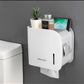 Wall-mounted toilet paper holder with a white finish, featuring a slot for toilet paper and a shelf for other bathroom supplies, such as a mobile phone and a plant.